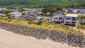 Una zona residencial costera con casas modernas, un litoral rocoso y colinas verdes al fondo.