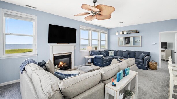 A living room with a fireplace, a large TV, and a ceiling fan. - Sunset Overlook, Spacious bay side top-floor condo with amazing views  (Ocean City)