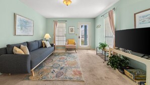 A living room with a sofa, a television, a patterned rug, and a door. - Condo steps to beach w/ daily attraction perks (Panama City Beach)