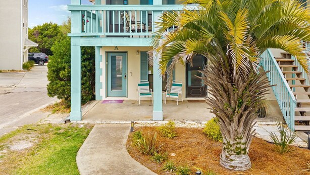 A two-story building with a balcony, a palm tree, and a staircase. - Condo steps to beach w/ daily attraction perks (Panama City Beach)