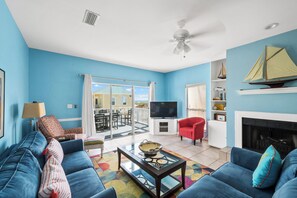 A living room with a blue sofa, a red armchair, a television, and a fireplace. - 3BR/2BA Fort Morgan Home | Sleeps 8 | Gulf Views & Bunkroom Fun (Gulf Shores)