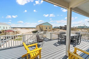 A wooden deck with outdoor seating, a covered area, and a view of the beach and buildings in the background. - 3BR/2BA Fort Morgan Home | Sleeps 8 | Gulf Views & Bunkroom Fun (Gulf Shores)
