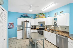 A kitchen with white cabinets, stainless steel appliances, and a blue wall with a 'Baja' sign. - 3BR/2BA Fort Morgan Home | Sleeps 8 | Gulf Views & Bunkroom Fun (Gulf Shores)