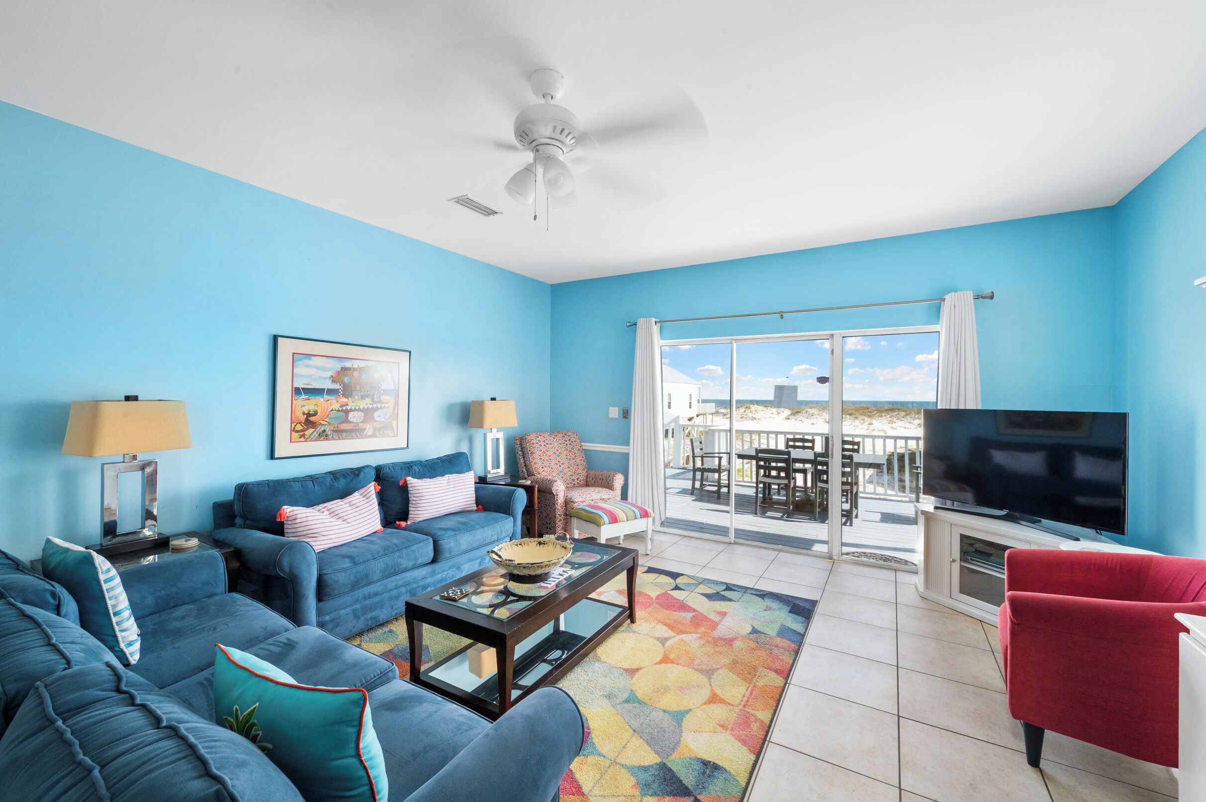 A living room with blue walls, a ceiling fan, a TV, and a balcony with a view.