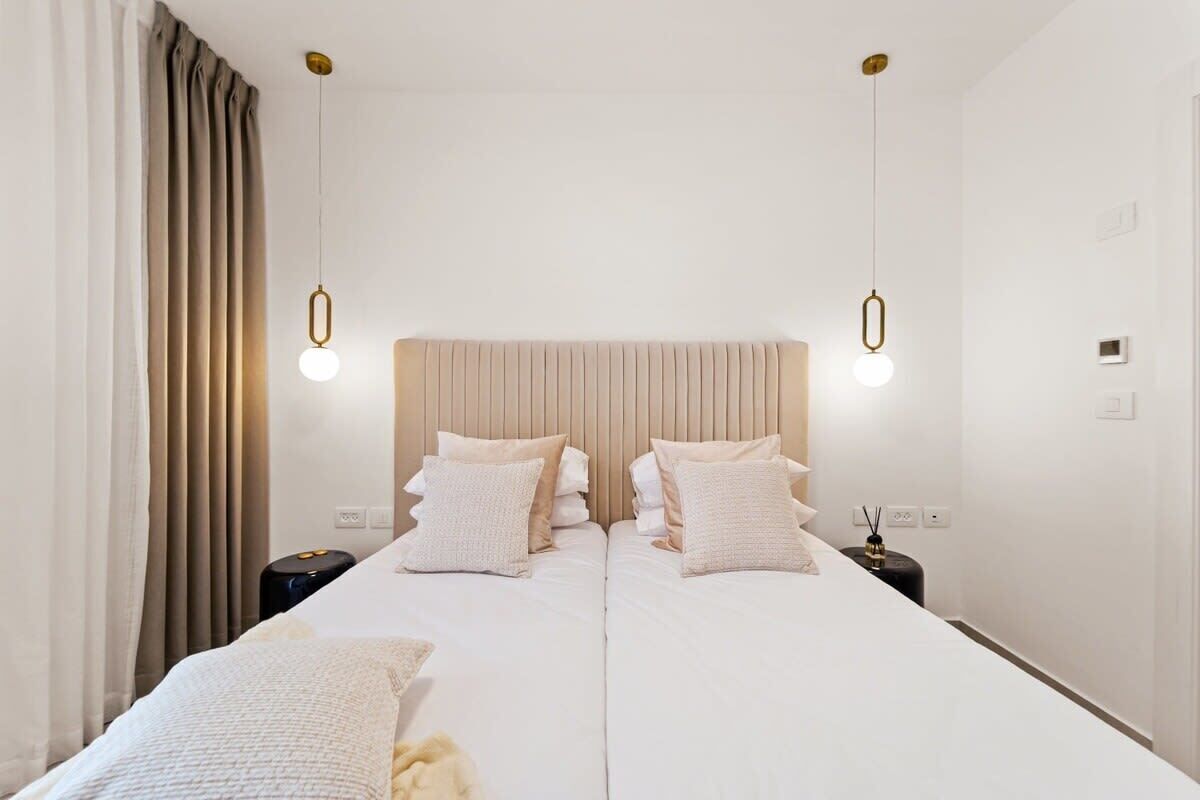 A double bed with a beige headboard, two bedside tables, and two pendant lights.