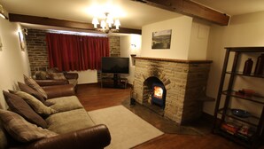 A cozy living room with a stone fireplace, leather sofa, and a television. - Idyllic cottage in Slaithwaite, stunning views, heart of the countryside (Upper Holme)
