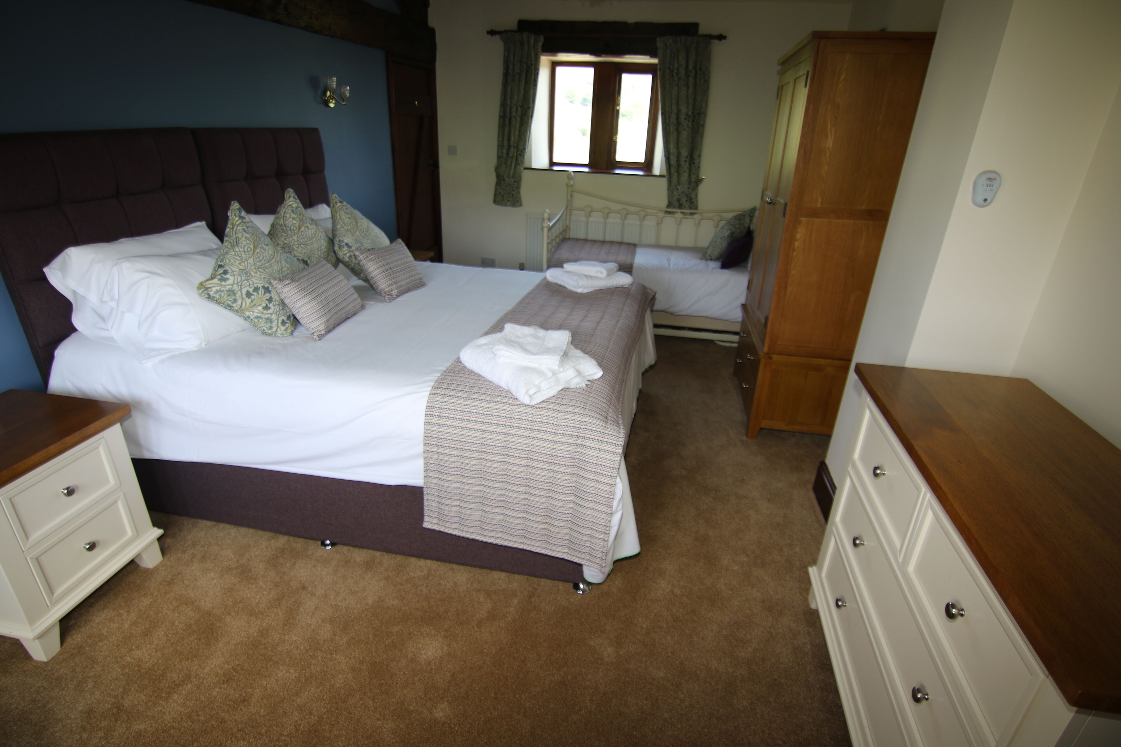A bedroom with a large bed, two bedside tables, a dresser, and a window with curtains.