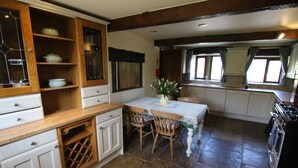 A kitchen with wooden cabinets, a dining table with chairs, and a stove. - Idyllic cottage in Slaithwaite, stunning views, heart of the countryside (Upper Holme)