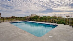 A rectangular swimming pool with a blue interior, surrounded by a concrete deck and a black metal fence. - Coastal Retreat: Elevator, Pool now open, Walk to Beach! (North Topsail Beach)