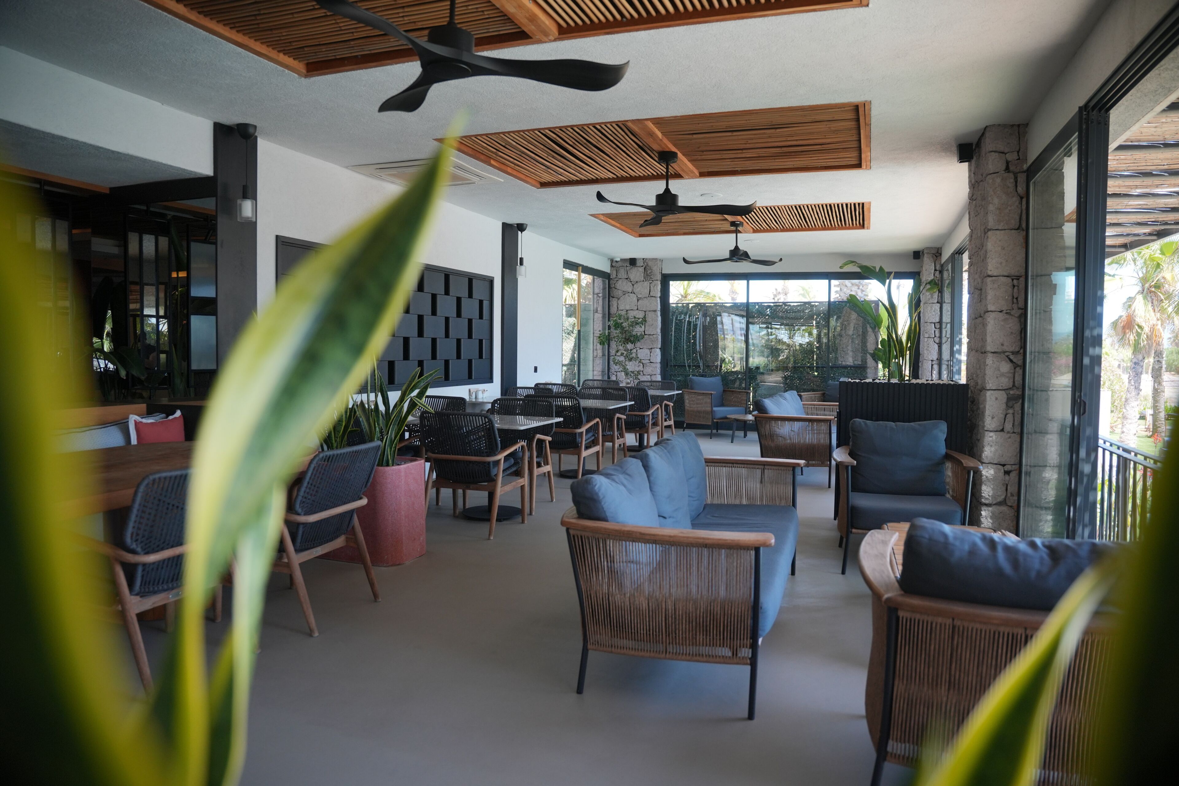 Un espacio interior moderno con ventiladores de techo, muebles de mimbre y ventanas amplias.