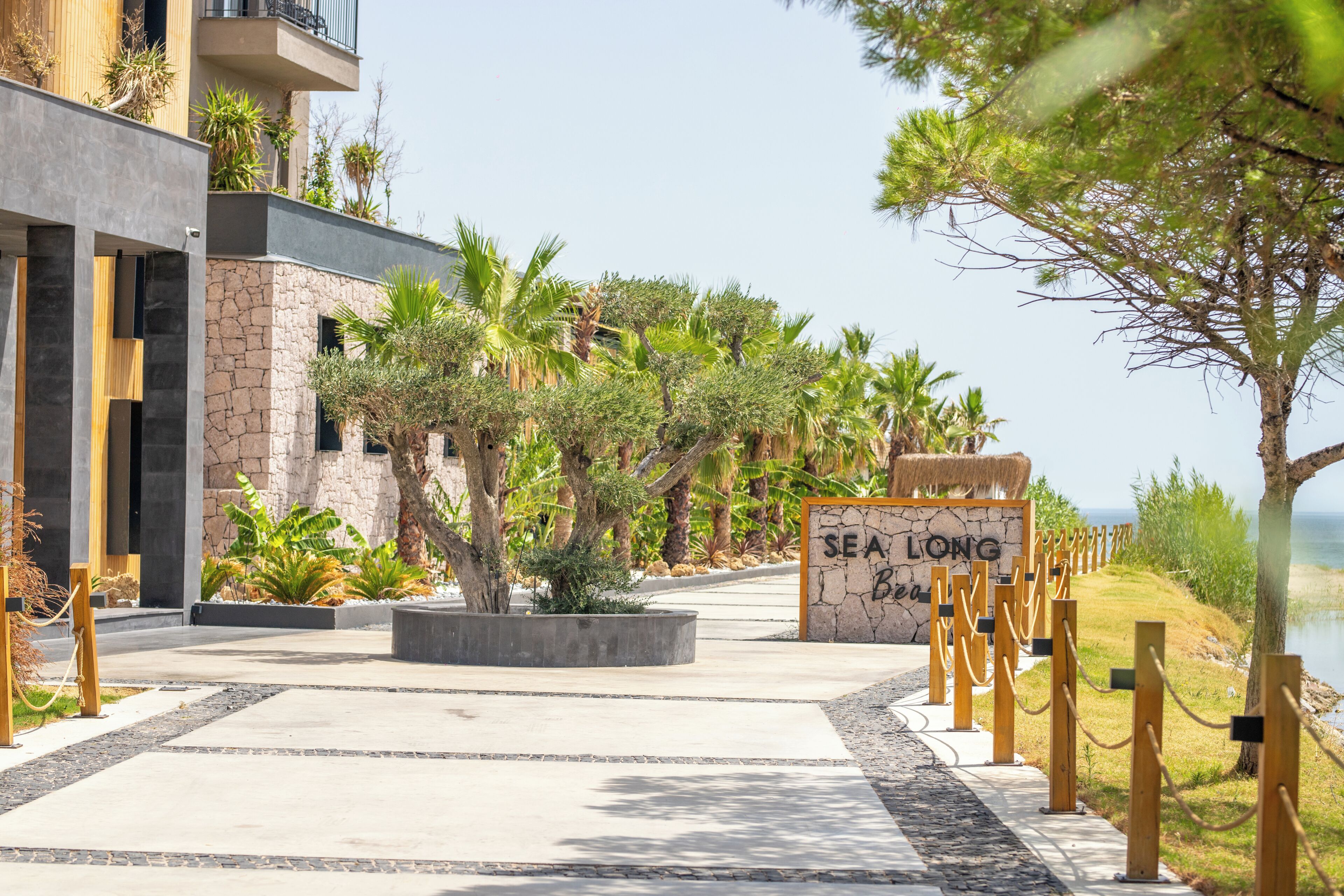 A modern building with a stone facade, a sign reading 'SEA LONG Beach,' and a pathway leading to the water.
