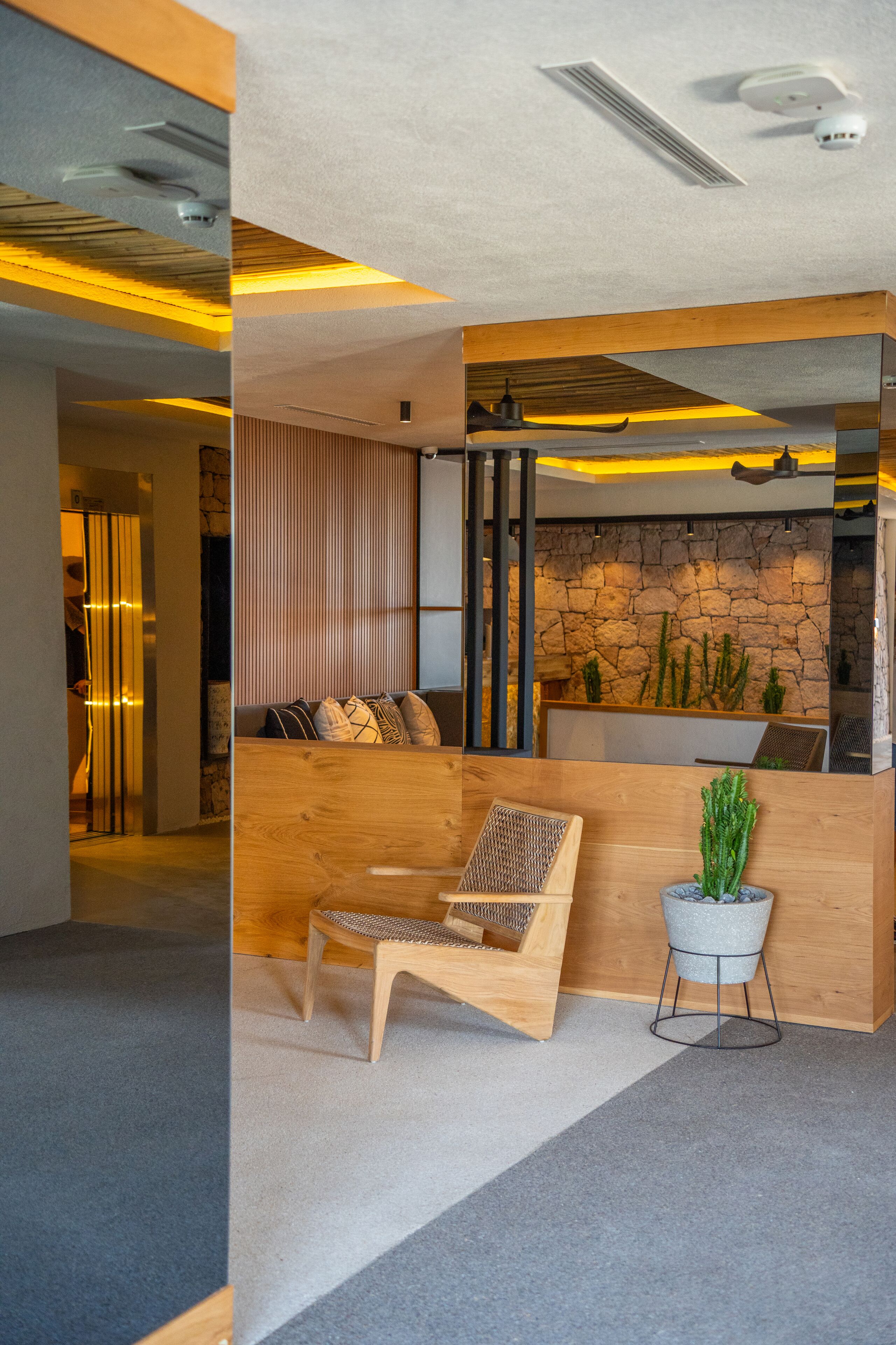 A reception area with a wooden reception desk, a seating area with a woven chair, a potted plant, and a stone wall with cacti.