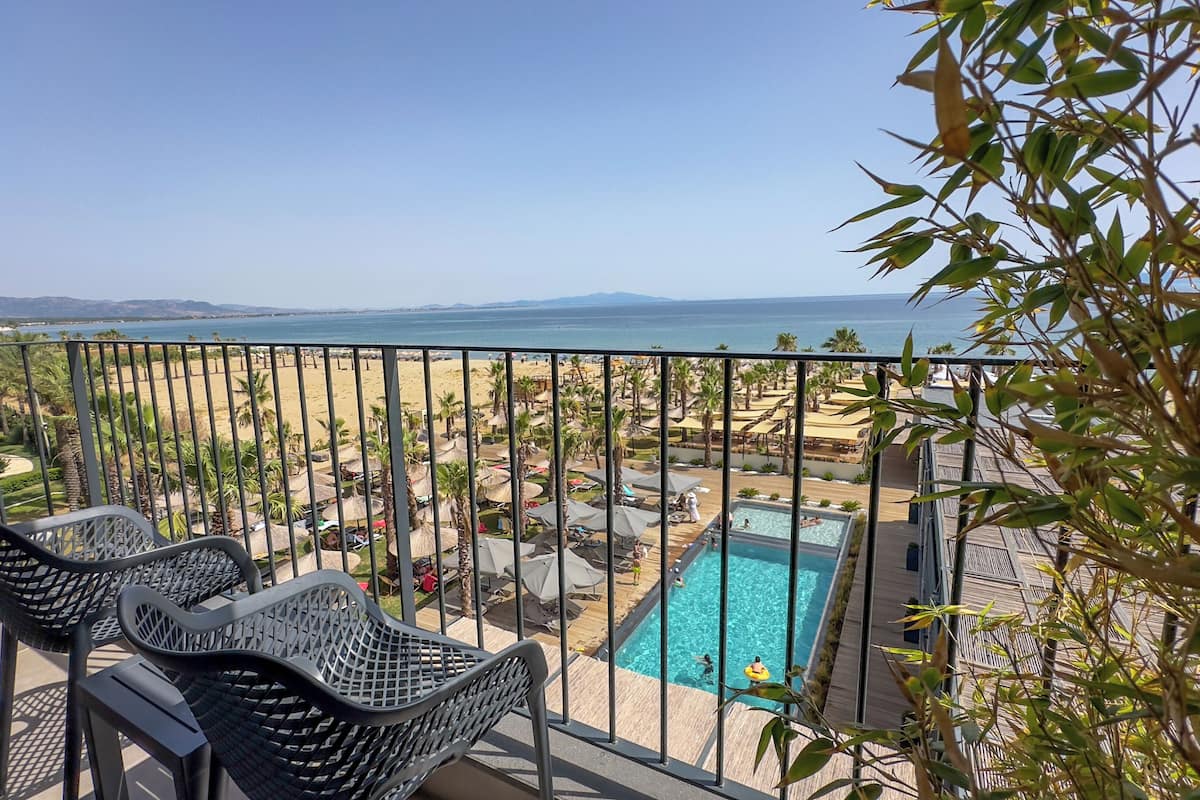 A balcony with a view of a beach, a pool, and palm trees.