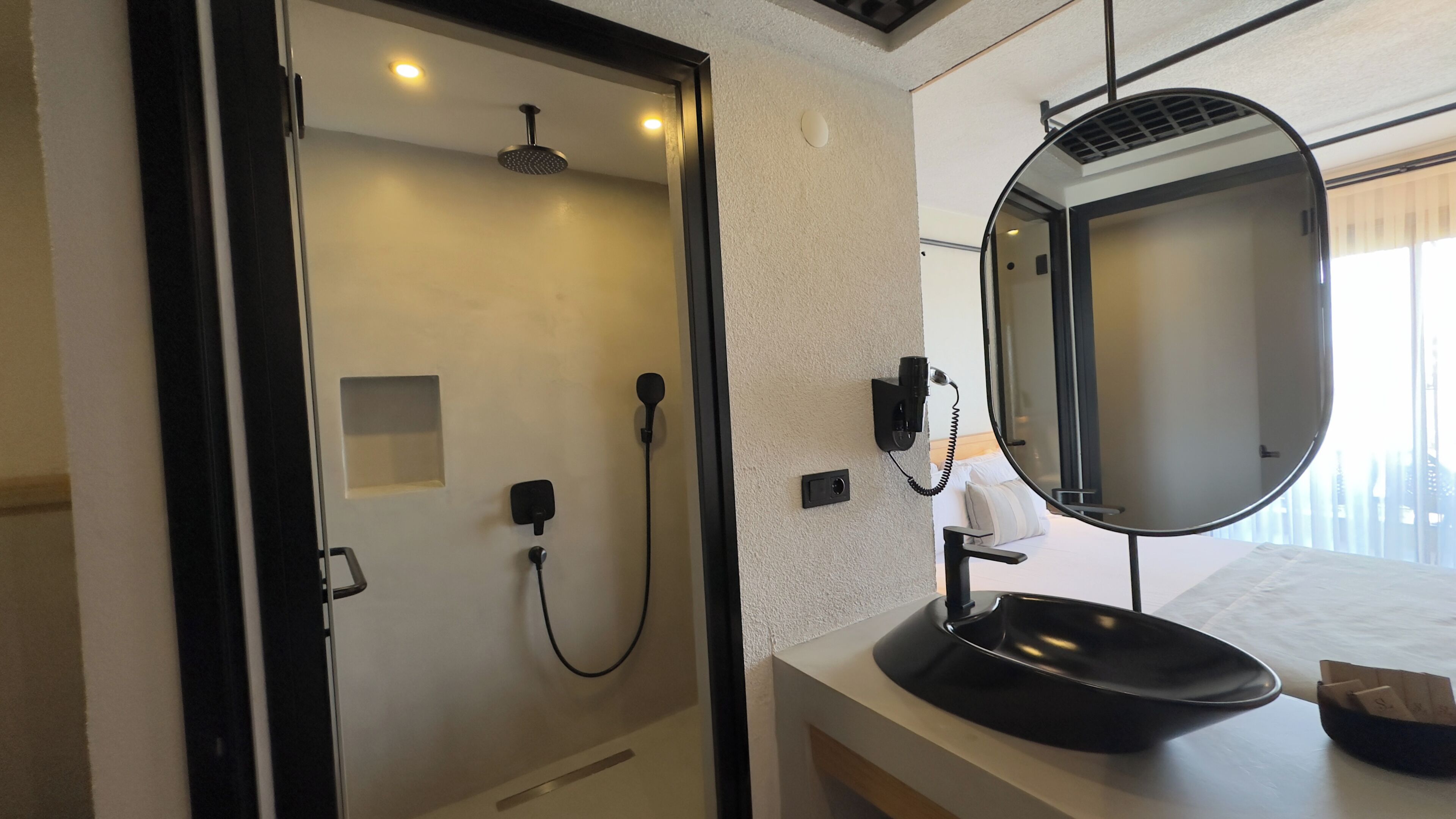 A bathroom with a shower, a sink, a mirror, and a telephone.
