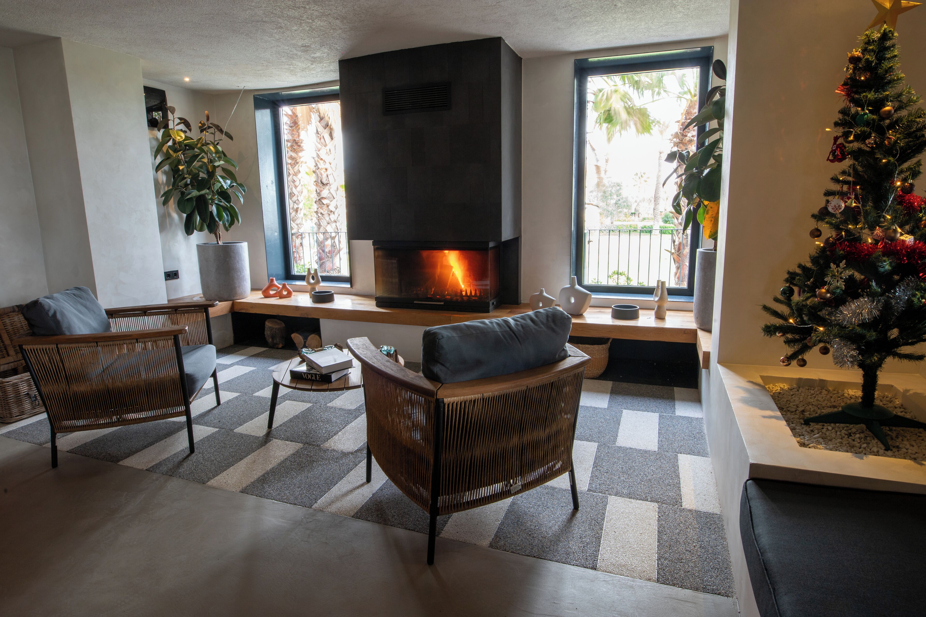 A modern living room with a fireplace, two wicker chairs, a coffee table, and a Christmas tree.