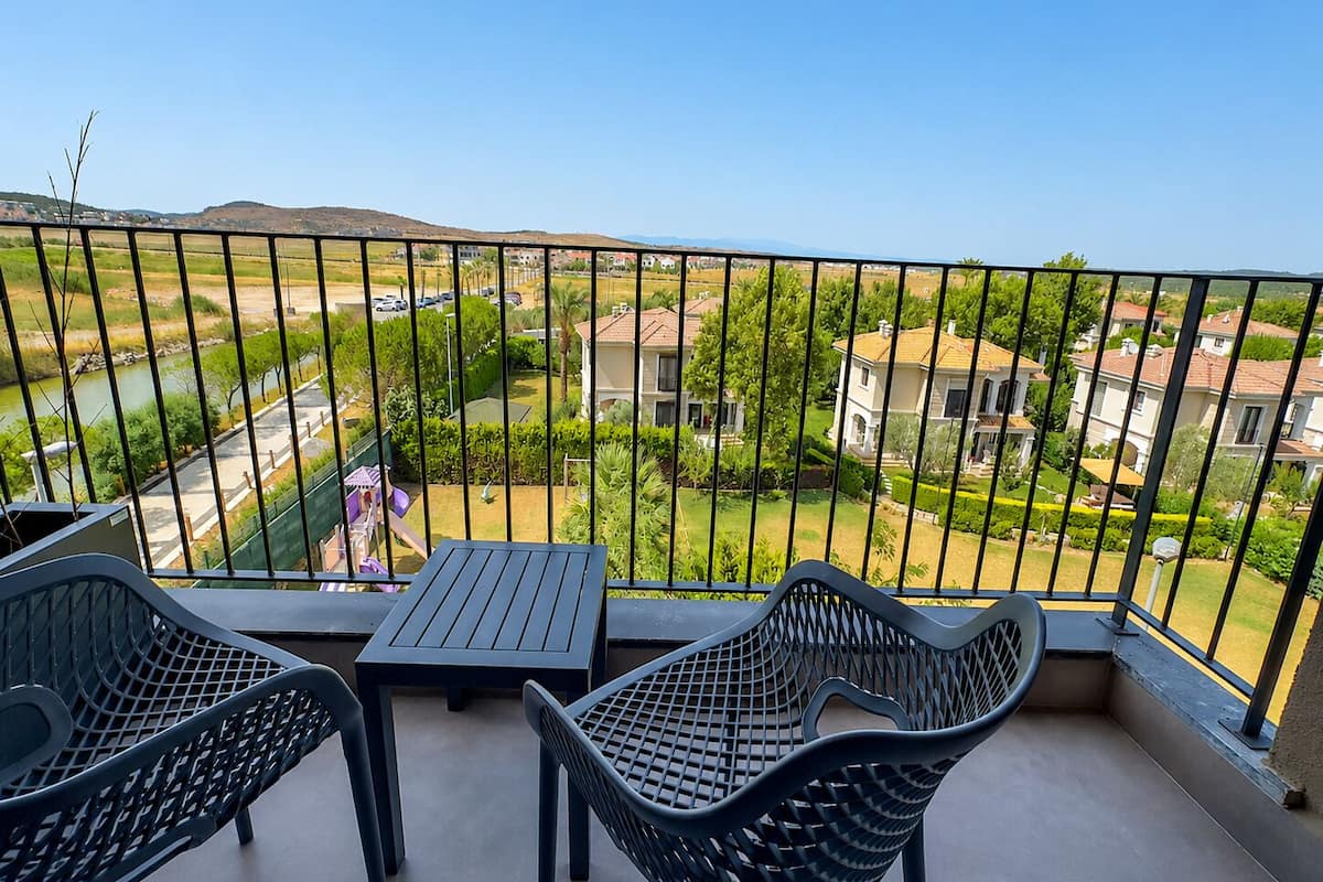 A balcony with a table and two chairs, overlooking a residential area with houses and greenery.