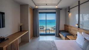 A modern hotel room with a large bed, a wooden desk, a TV, and a balcony with a view of the beach and ocean. - Ayvalık Sea Long (Ayvalik)