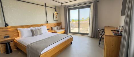 A modern hotel room with a wooden bed, a desk, and a balcony with a view.