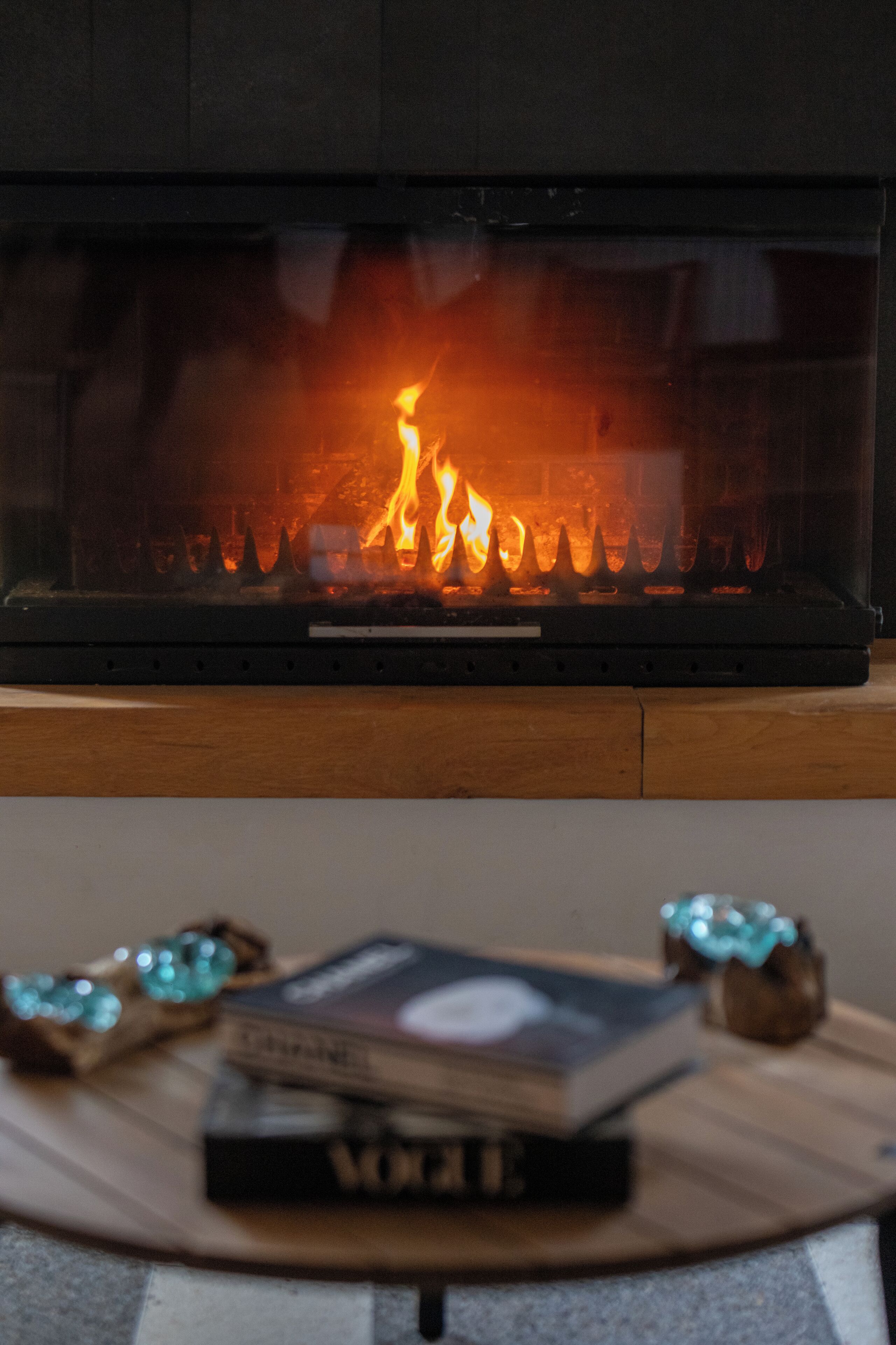 A fireplace with a fire, a book, and decorative items on a wooden table.
