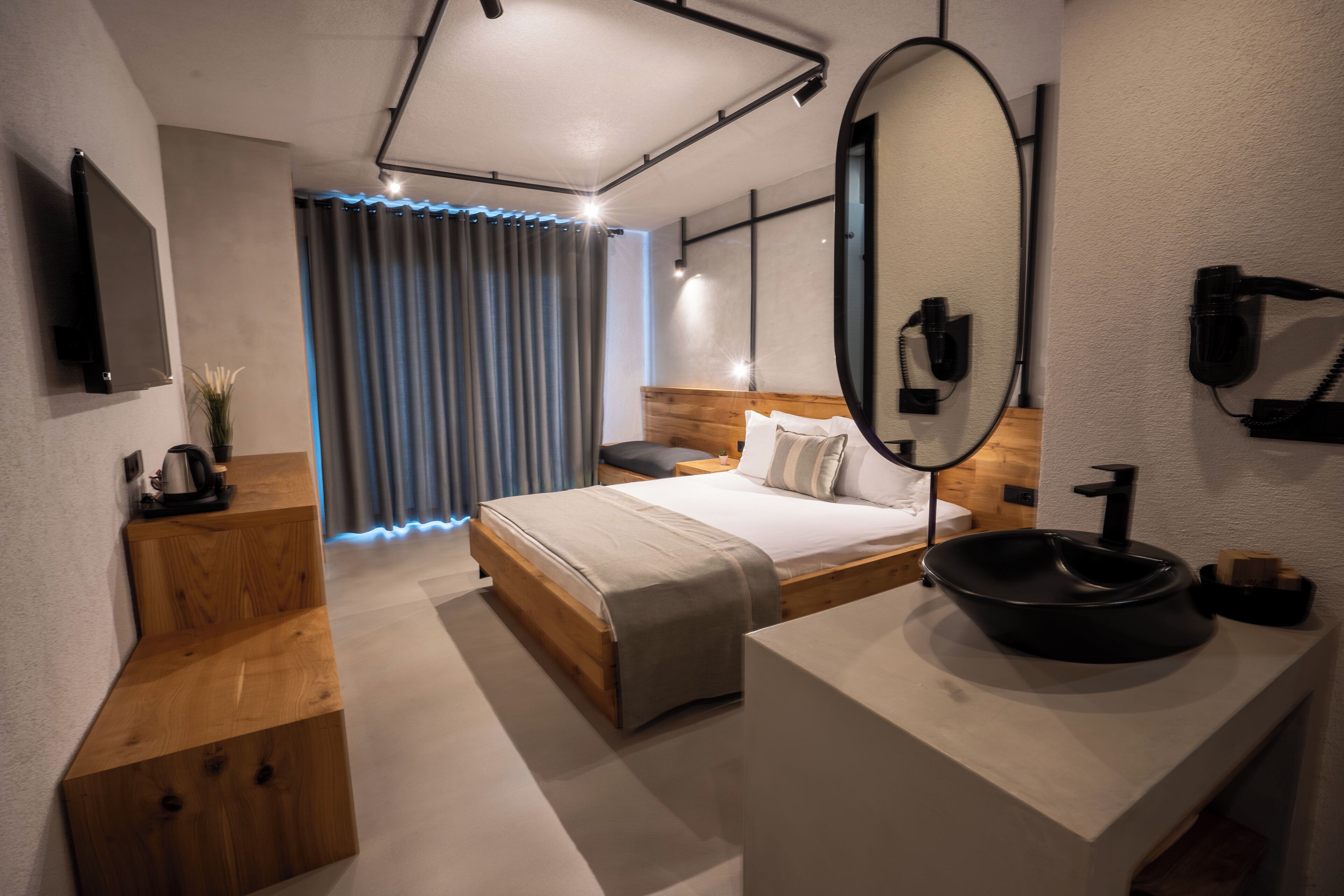 A modern hotel room with a wooden bed, a large mirror, a round black sink, and a wooden nightstand.