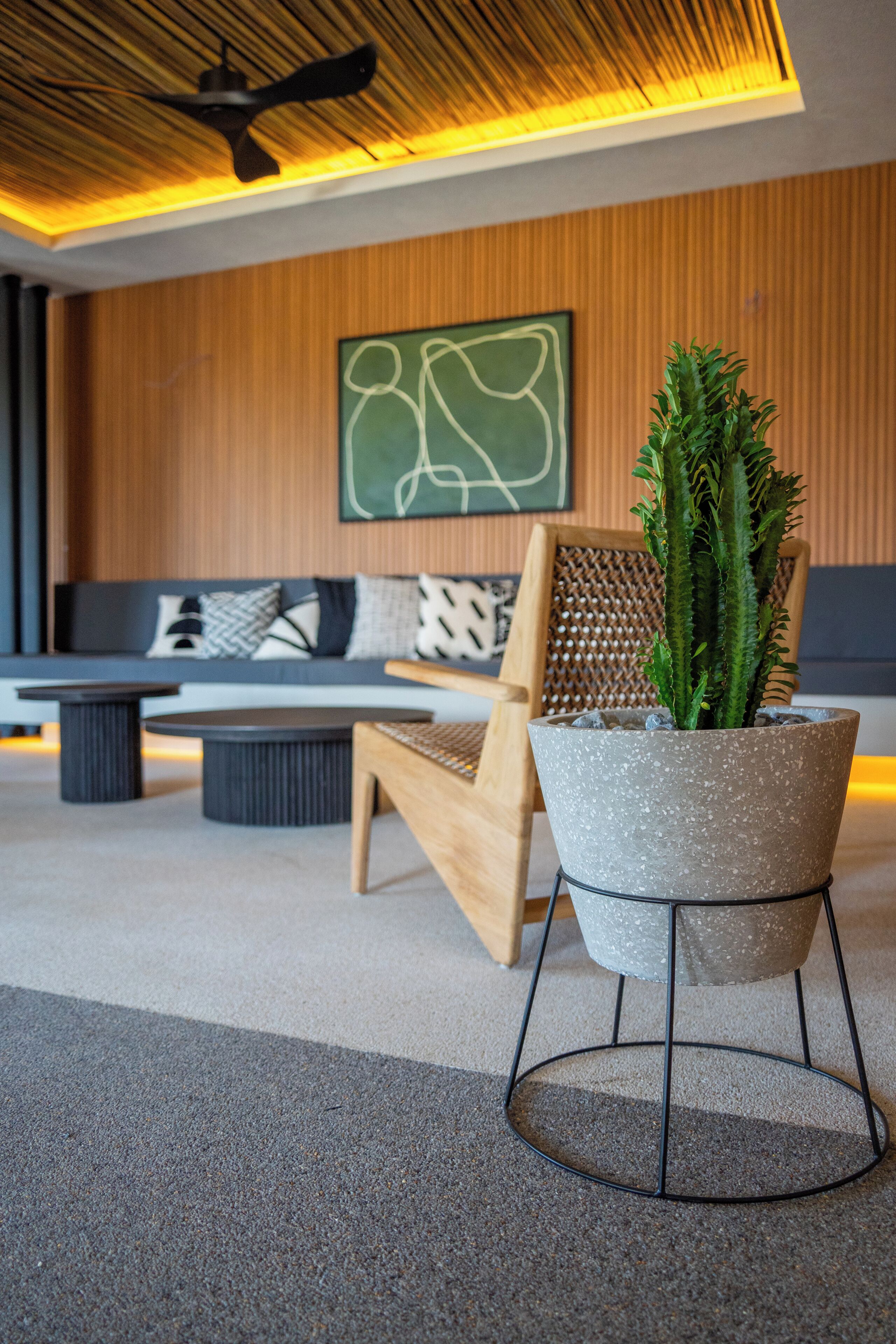 Una sala de estar moderna con techo de madera, ventilador de techo, sofá con cojines estampados, una mesa de centro y una planta en maceta.