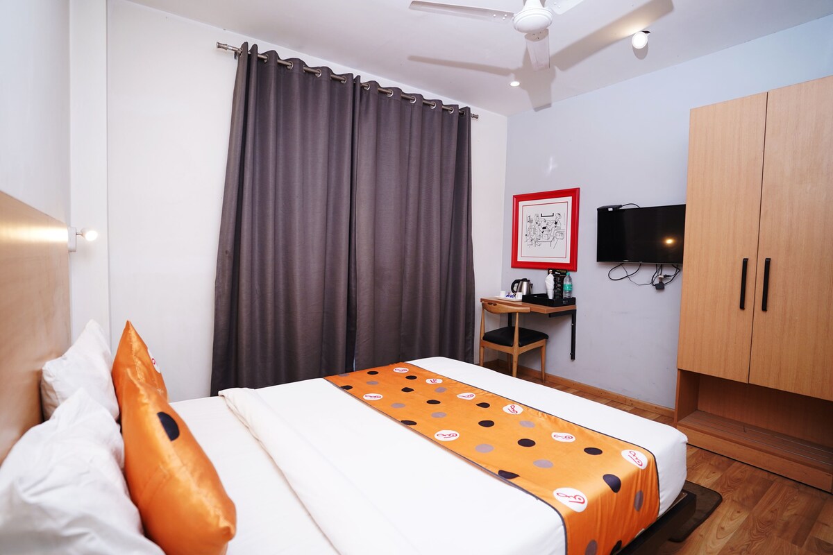 A hotel room with a bed, curtains, a desk with a chair, a television, and wooden cabinets.