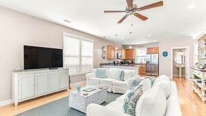 A spacious living room with a white sofa, a coffee table, and a flat-screen TV. - Peach Coral | Mid Island, Game Room, Walk to Beach (Tybee Island)