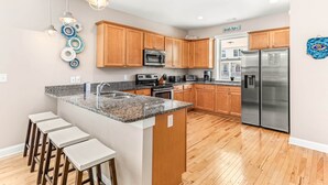 A modern kitchen with wooden cabinets, stainless steel appliances, and a granite countertop. - Peach Coral | Mid Island, Game Room, Walk to Beach (Tybee Island)