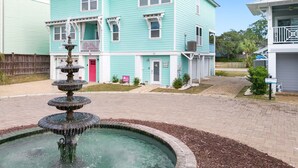 A turquoise two-story building with a front porch and a fountain in the courtyard. - Peach Coral | Mid Island, Game Room, Walk to Beach (Tybee Island)