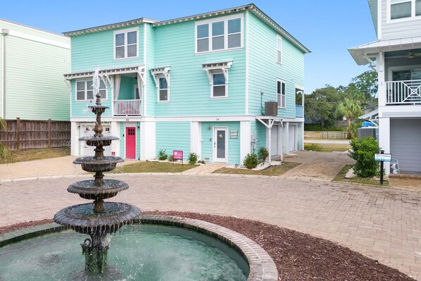 A turquoise two-story building with a front porch and a fountain in the courtyard. - Peach Coral | Mid Island, Game Room, Walk to Beach (Tybee Island)
