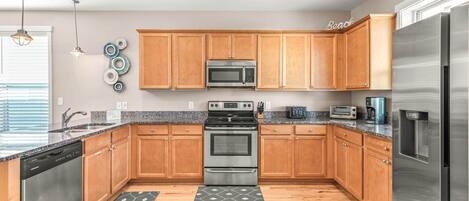 A modern kitchen with wooden cabinets, stainless steel appliances, granite countertops, and a herringbone-patterned rug.