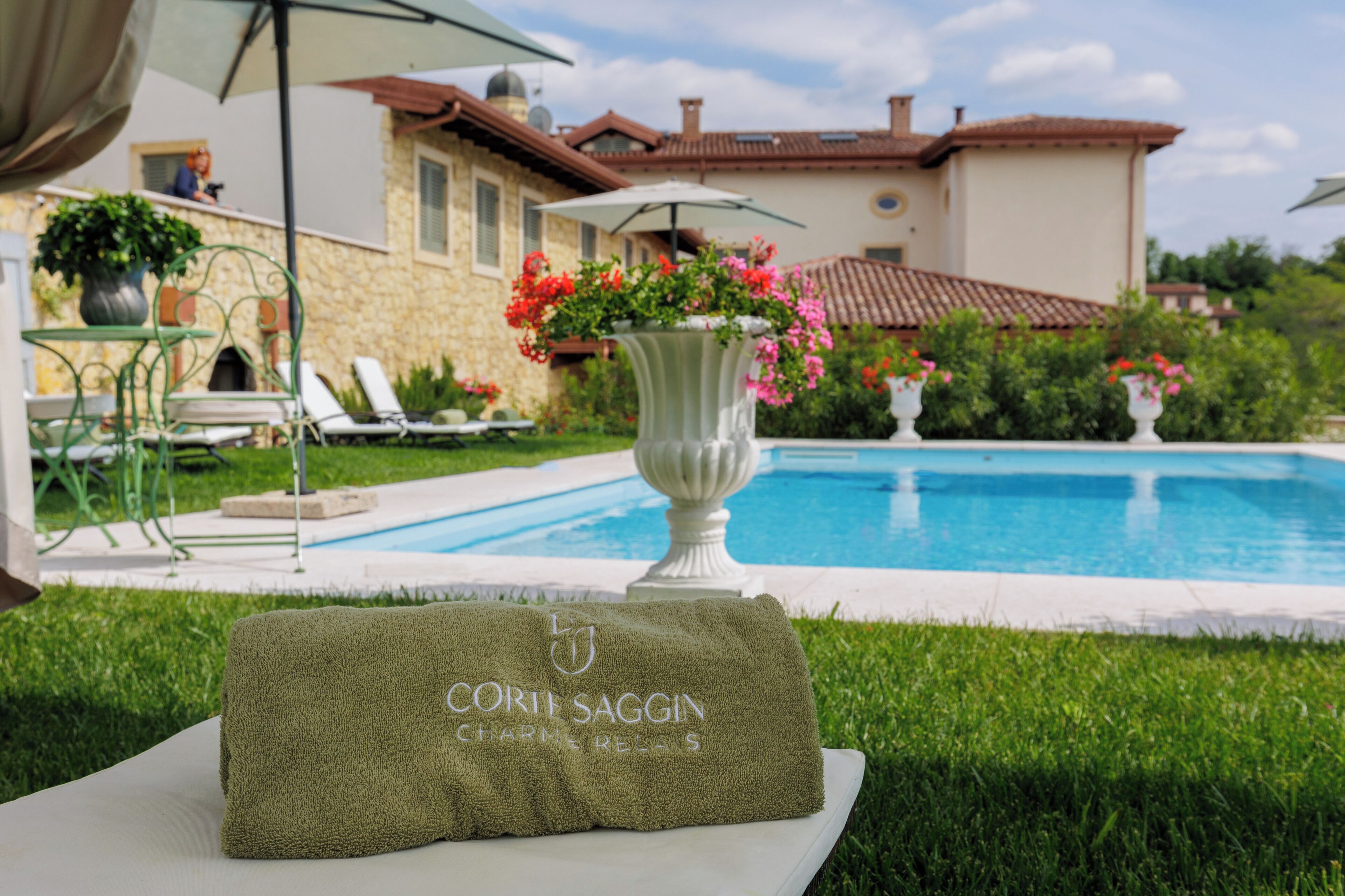 Un espace aménagé au bord de la piscine, avec un fauteuil de relaxation, une table avec une serviette, et une maison en arrière-plan.