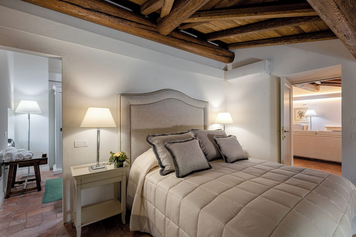 A bedroom with a large bed, bedside lamps, a nightstand, and a wooden ceiling.