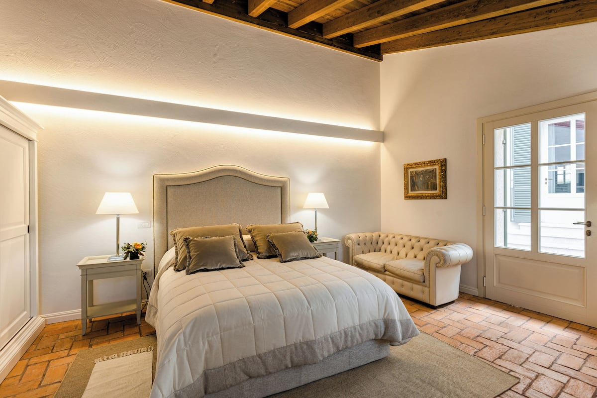 A bedroom with a large bed, two bedside tables with lamps, a chair, and a door with windows.