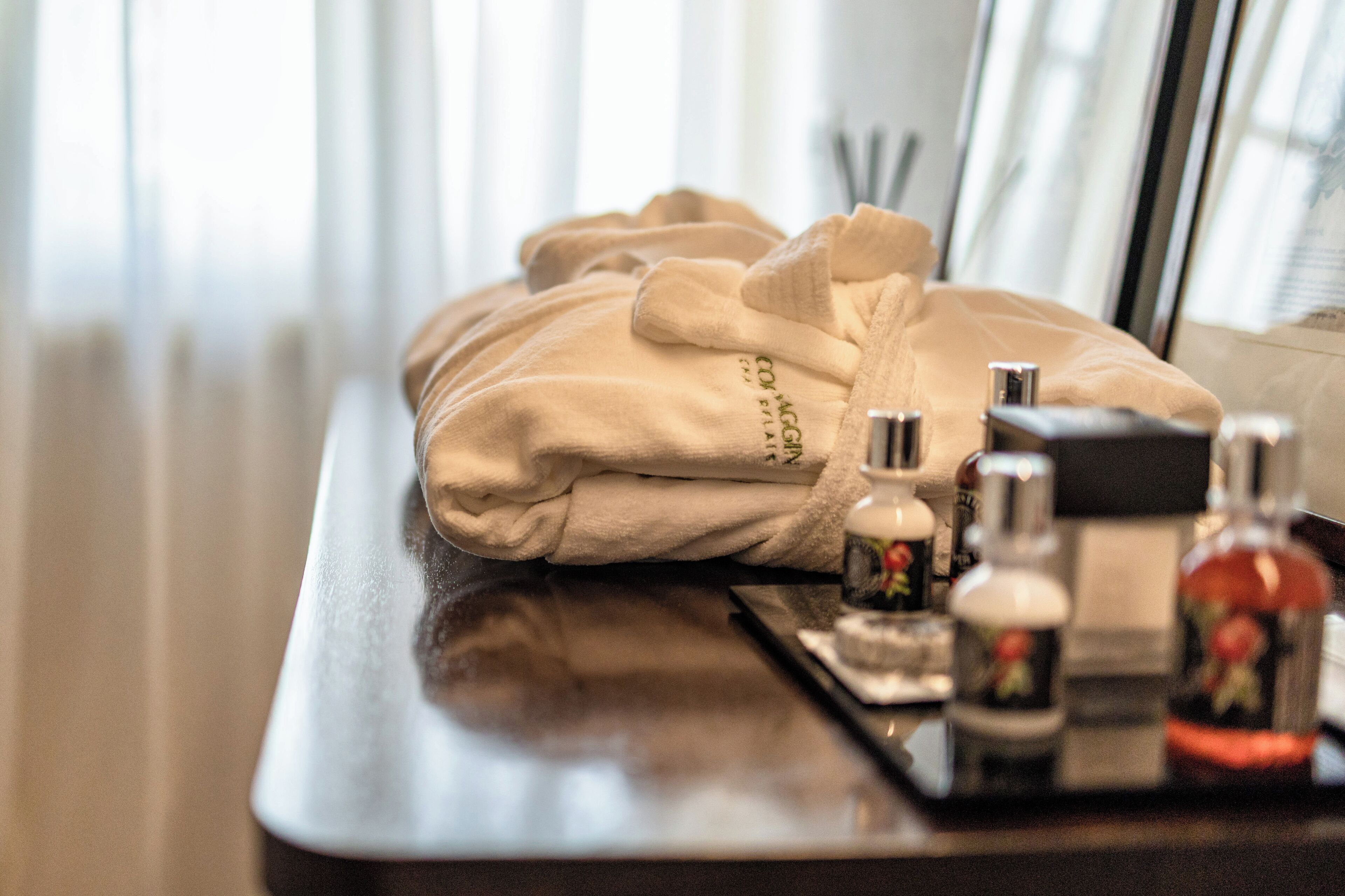 Un peignoir beige, soigneusement plié, est posé sur un plateau en bois, accompagné de produits de toilette, notamment un flacon de lotion et un flacon de shampoing.