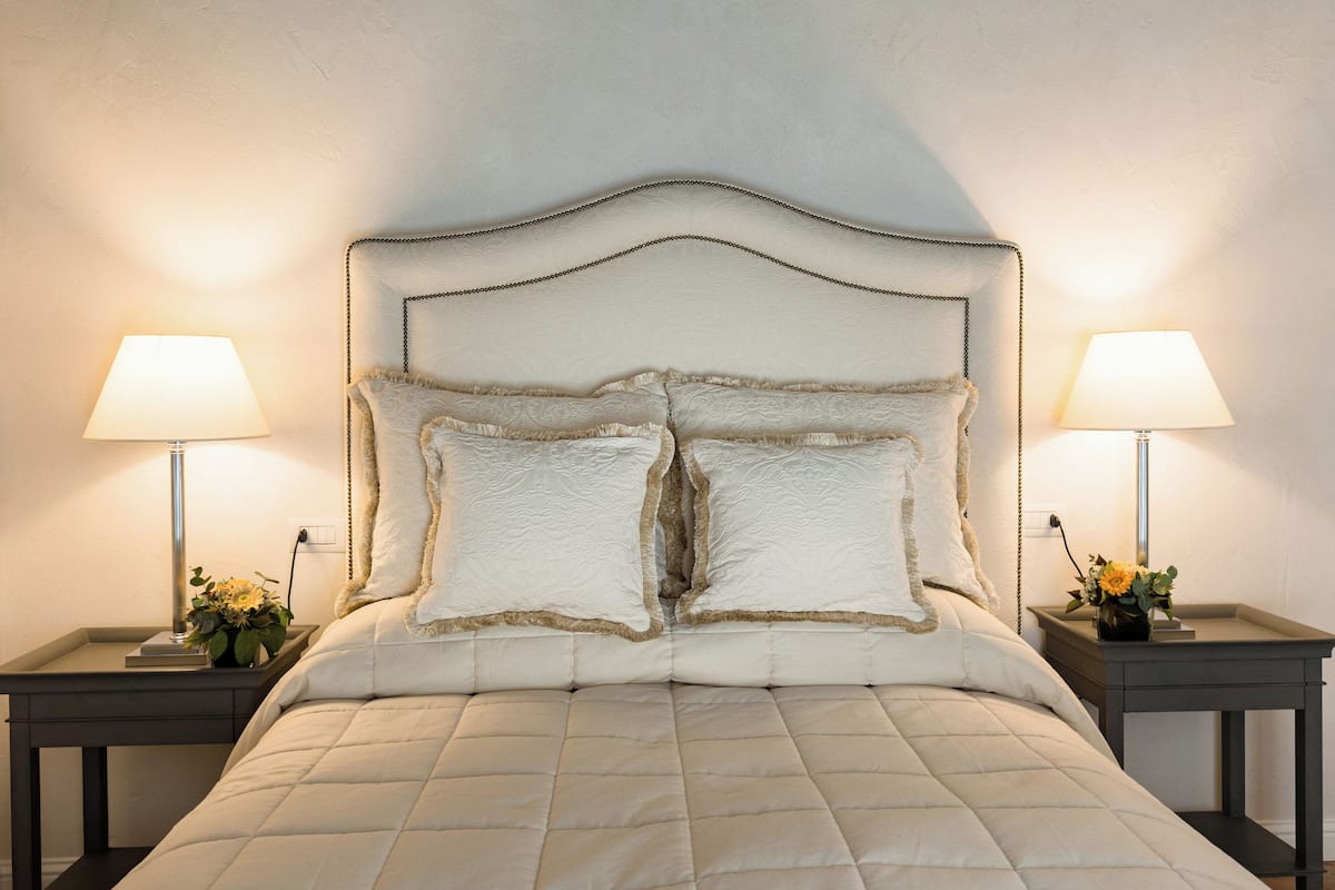 A neatly made bed with a tufted headboard, flanked by two bedside tables with lamps and small flower arrangements.