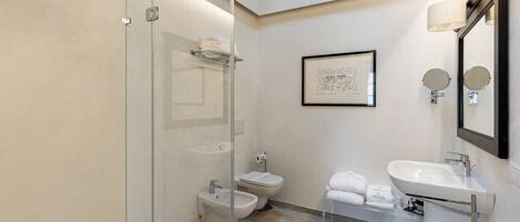 A modern bathroom with a glass shower enclosure, a bidet, a toilet, and a sink with a mirror.