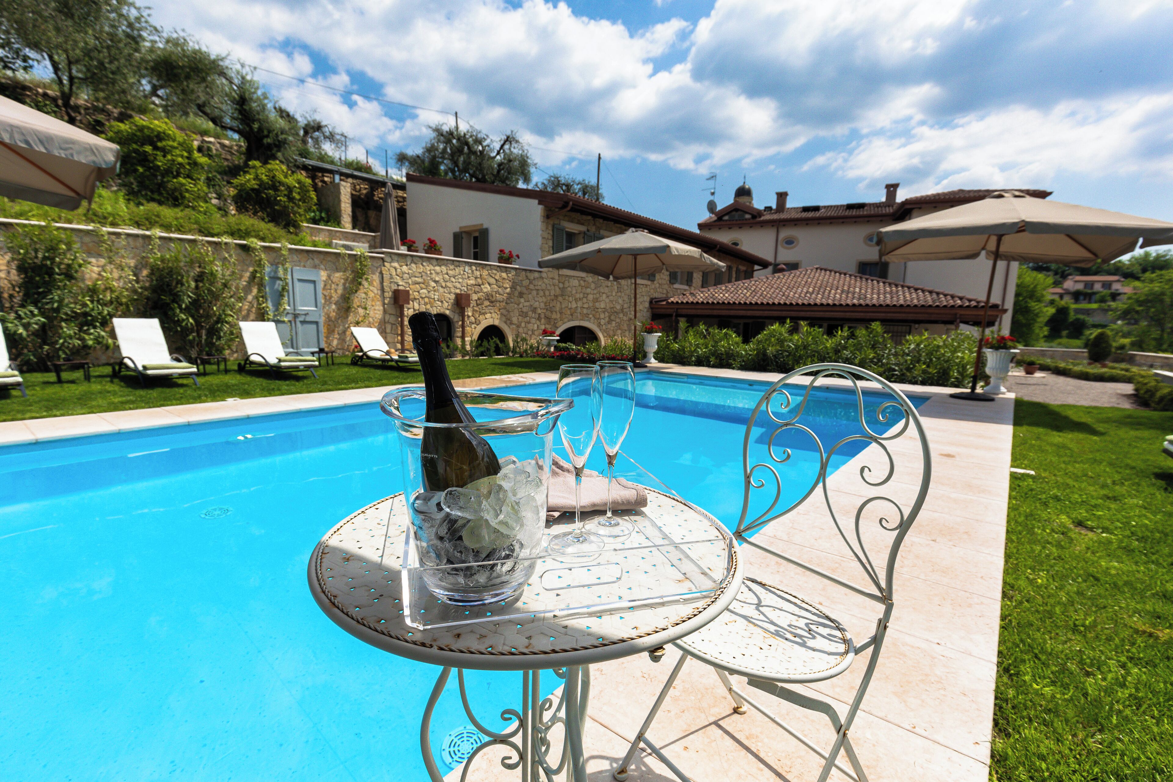 Un espace piscine avec des chaises longues, une table avec une bouteille et des verres, et un mur en pierre.