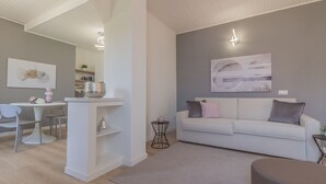 Un salon moderne avec un canapé blanc, un tapis gris et un coin repas comprenant une table et des chaises blanches.