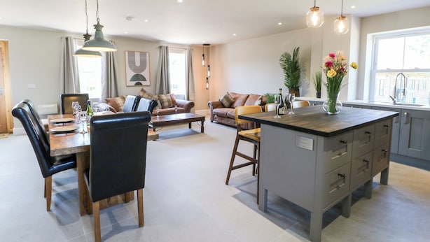 A modern kitchen with a central island, dining area with chairs and a table, and a living area with sofas and a coffee table. - The Workshop (Northallerton)