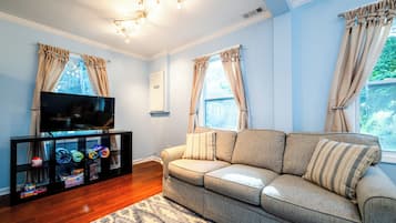 A living room with a sofa, a TV on a stand, and a shelf with toys.