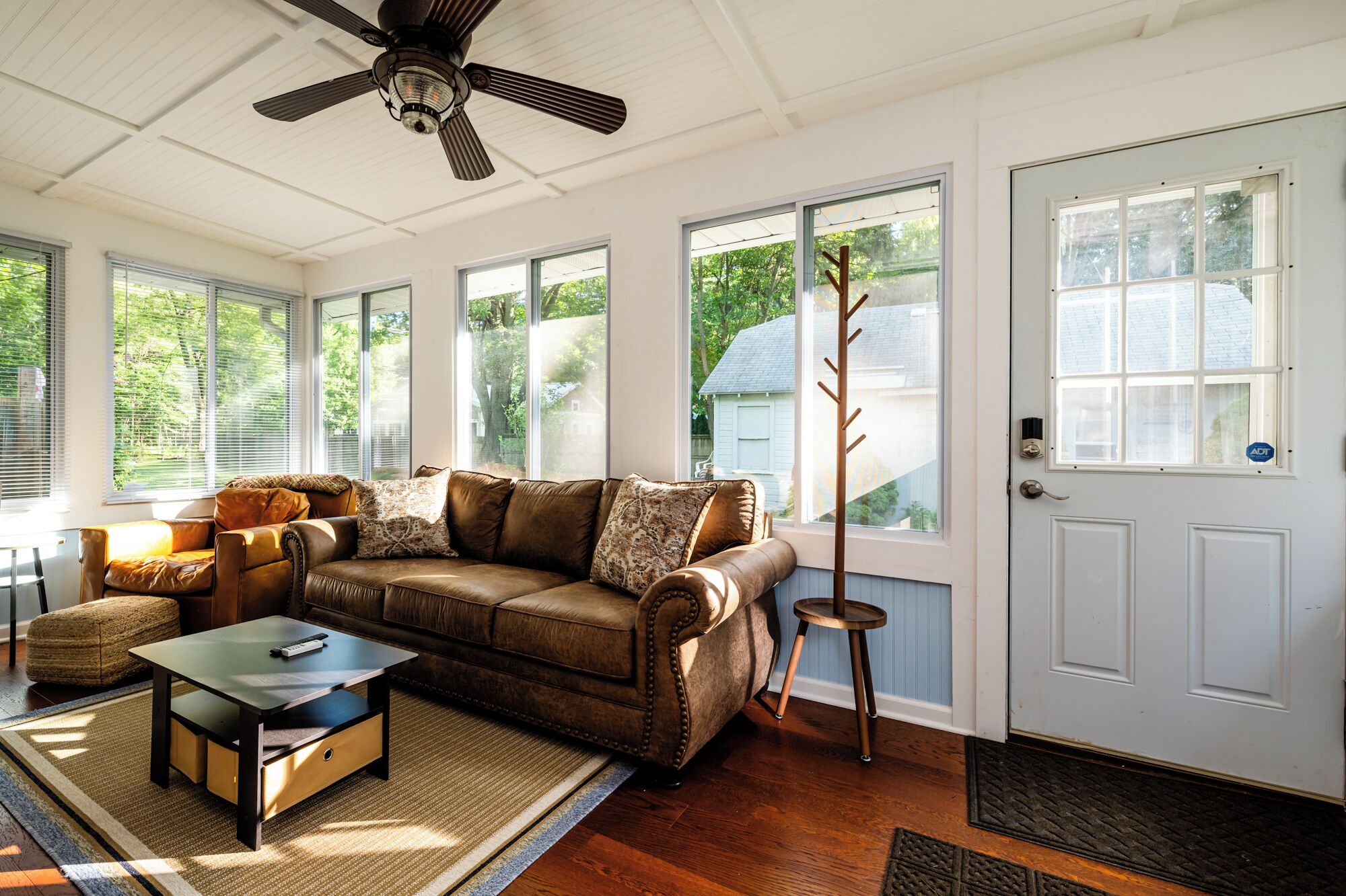 A cozy living room with a brown leather sofa, a wooden coffee table, and a ceiling fan.