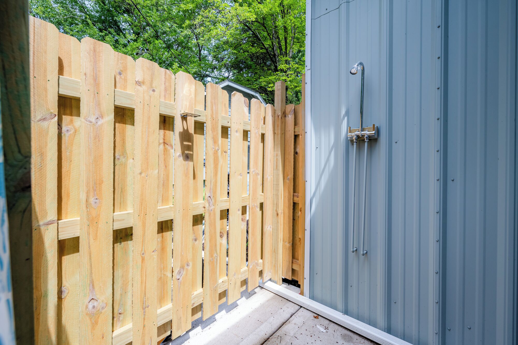 A wooden fence with a metal gate, a grey metal shed, and a concrete floor.