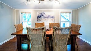 A dining room with a wooden table and wicker chairs, large windows, and a ceiling light fixture. - 2027 OPEN! 3 Night Min~Union Pier Home Close To Beach and Downtown! (Union Pier)