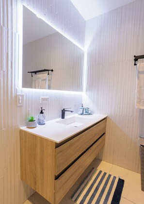A modern bathroom with a wooden vanity, a large mirror, a white sink, and a striped rug.