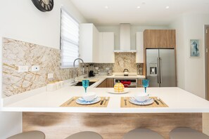 Une cuisine moderne avec des meubles blancs, un pare-feu en marbre et un îlot central agrémenté de deux verres bleus.