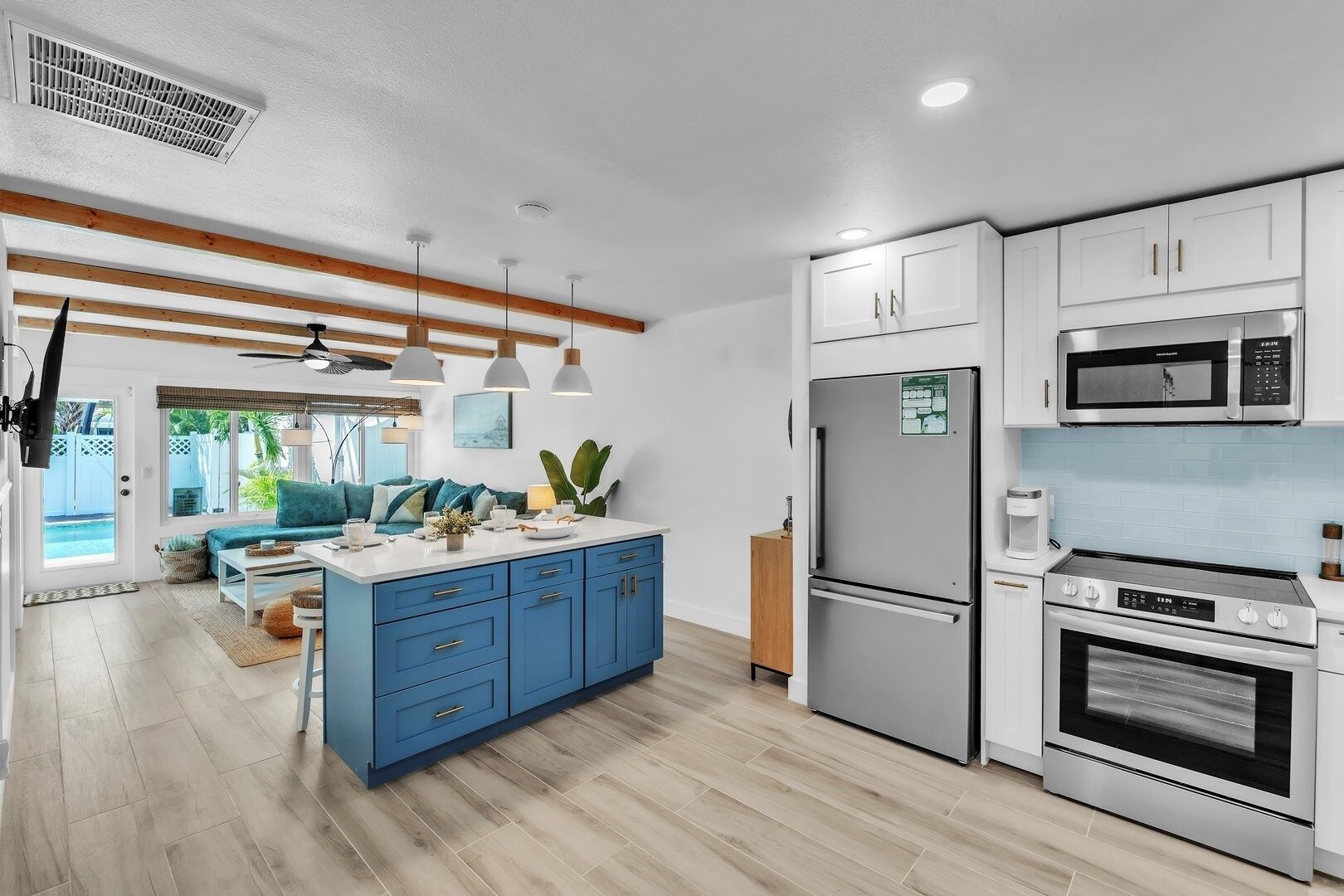 A modern kitchen with white cabinets, a blue island, stainless steel appliances, and a view of the outdoors.