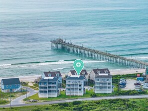 A coastal area with a pier extending into the sea, a row of beachfront buildings, and a road leading to the beach. - Beach Badger #147 - Rate Reduction! Ocean View Private Hot Tub, Dog Friendly! (North Topsail Beach)