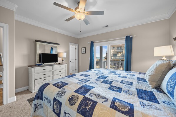 A bedroom with a bed, a ceiling fan, a dresser, a television, and a view of the outside balcony. - Beach Badger #147 - Rate Reduction! Ocean View Private Hot Tub, Dog Friendly! (North Topsail Beach)
