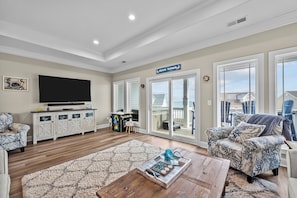 A spacious living room with a large flat-screen TV, a wooden coffee table, and a patterned armchair. - Beach Badger #147 - Rate Reduction! Ocean View Private Hot Tub, Dog Friendly! (North Topsail Beach)